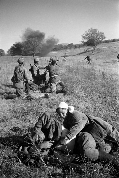 Санитарка перевязывает тяжелораненого на поле боя. На втором плане стрельба из миномета. Сталинградская битва, 1942 г.